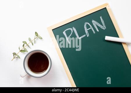 Piano lavagna scritta con tazza di caffè su sfondo bianco. Vista dall'alto Foto Stock