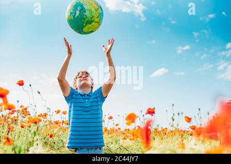 Ragazzo la cattura del mondo mentre in piedi nel campo di papavero contro sky sulla giornata di sole Foto Stock