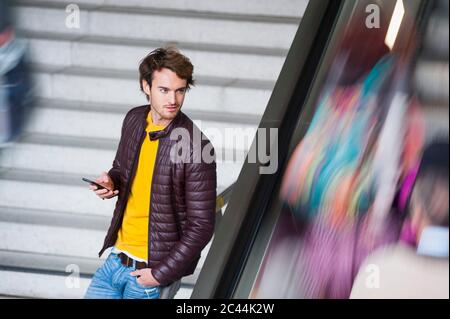 Ritratto di giovane uomo con smartphone in attesa alle scale Foto Stock
