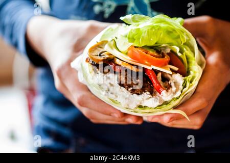 Le mani della persona che tiene il carburatore basso burger con bun insalata di verdure arrosto e salsa tzatziki Foto Stock