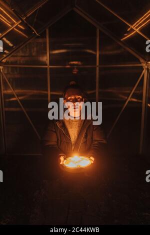 Giovane donna con candele accese in piastra a serra durante la notte Foto Stock