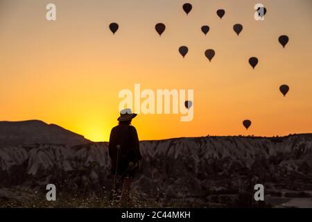 Vista posteriore di silhouette giovane donna guardando i palloni ad aria calda mentre in piedi sulla terra a Goreme, Cappadocia, Turchia Foto Stock