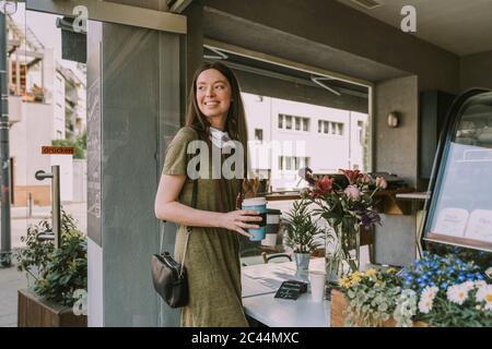 Donna sorridente con maschera a faccia in giù che tiene due caffè da asporto Foto Stock