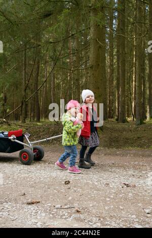 Due piccole sorelle che tirano il trolley sulla pista forestale Foto Stock