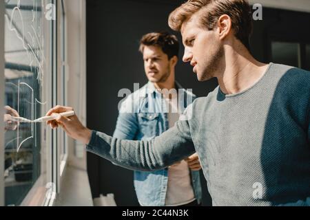 Grafico di disegno di giovane uomo sulla finestra dell'ufficio, con il collega che guarda Foto Stock