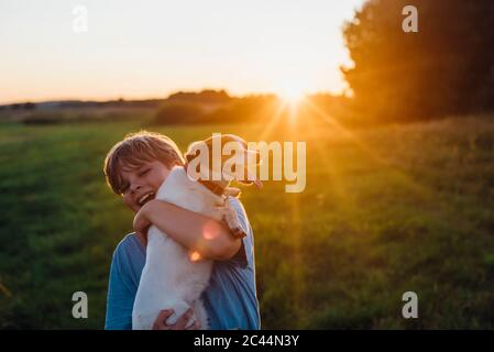 Giocoso ragazzo con cane sul campo durante il tramonto, Polonia Foto Stock