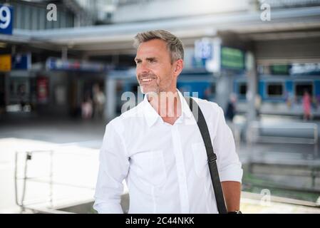 Uomo d'affari sorridente che guarda via mentre si trova alla stazione ferroviaria Foto Stock