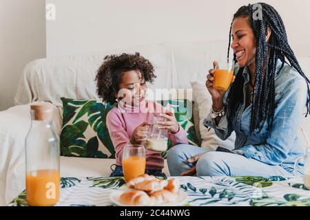 Madre felice e sua figlia piccola che beve frullato e succo a casa Foto Stock