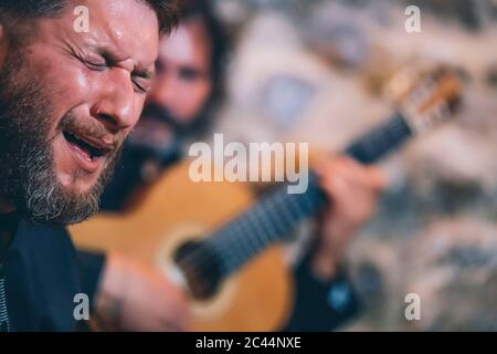 Primo piano di uomo con occhi chiuso cantando mentre il chitarrista suona la chitarra in background Foto Stock