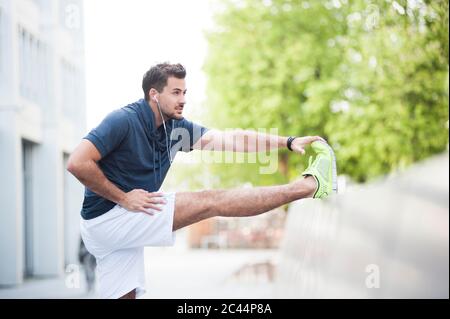 Giovane uomo che stende la gamba sul muro in città Foto Stock