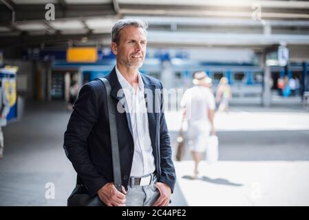 Uomo d'affari sorridente che guarda via mentre si trova alla stazione ferroviaria Foto Stock