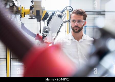 Esperto sicuro che guarda il braccio robotico in una fabbrica automatizzata Foto Stock