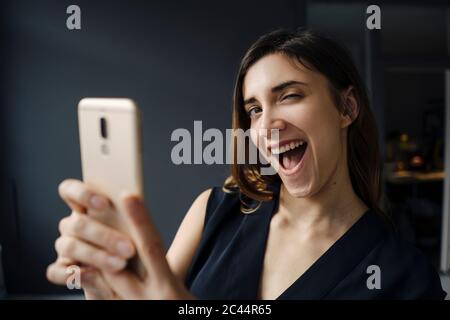 Ritratto di giovane donna con smartphone che tira volti divertenti Foto Stock