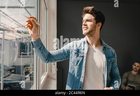 Giovane uomo che gioca tic-tac-toe sulla finestra dell'ufficio Foto Stock