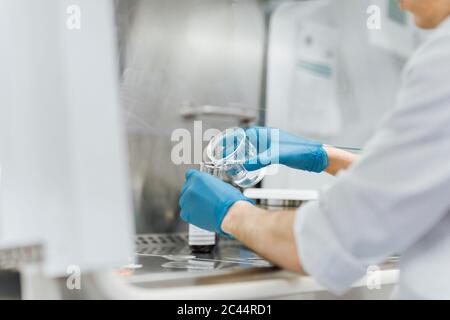 Giovane tecnico maschile che versa il prodotto chimico dal becher mentre si svolge la ricerca in laboratorio Foto Stock