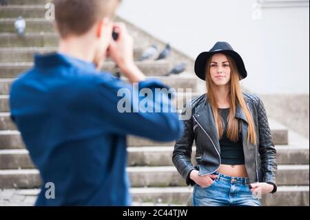 Uomo che fotografa una donna alla moda con la fotocamera sui gradini della città Foto Stock