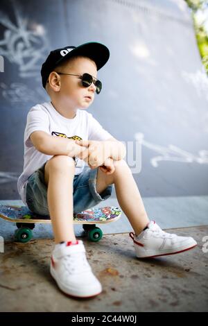 Ragazzo con un skate in un parco di skate. Il ragazzo è seduto su uno skateboard. Foto Stock