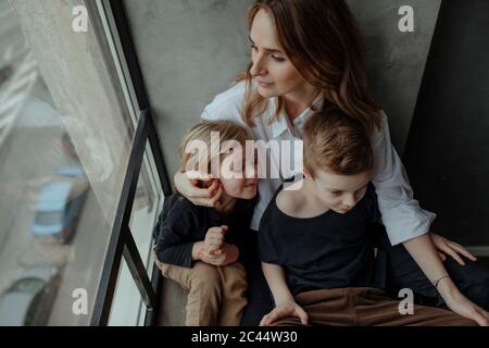 Vista ad alto angolo della donna seduta con i figli accanto alla finestra a casa Foto Stock