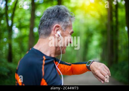 Vista laterale di un uomo sorridente che guarda un orologio intelligente nel parco Foto Stock