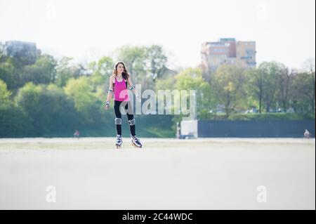 Giovane donna inline pattinare a terra in parco durante la giornata di sole Foto Stock