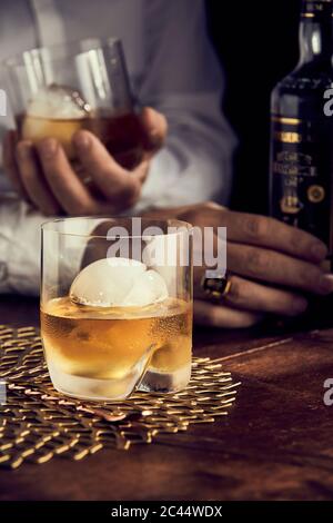 Scotch con ghiaccio, mani in background Foto Stock