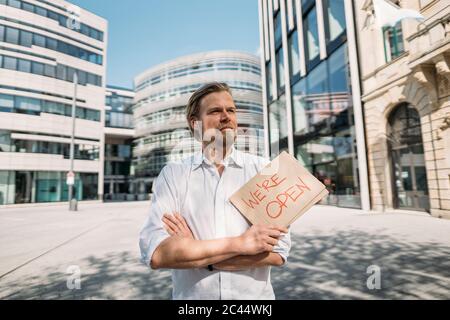 Negoziante in possesso di cartone con annuncio di apertura in città Foto Stock