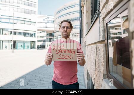 Negoziante in possesso di cartone con annuncio di apertura in città Foto Stock