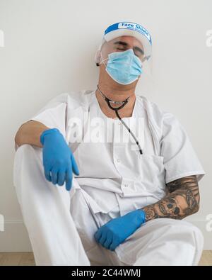 Uomo esausto in abbigliamento protettivo seduto sul pavimento Foto Stock