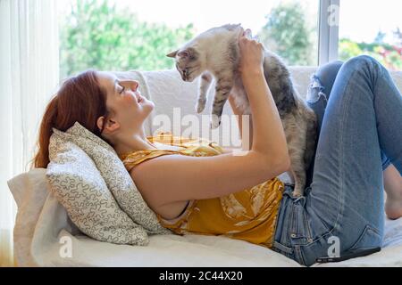 Giovane donna che si steso sul divano a casa tenendo il suo gatto Foto Stock