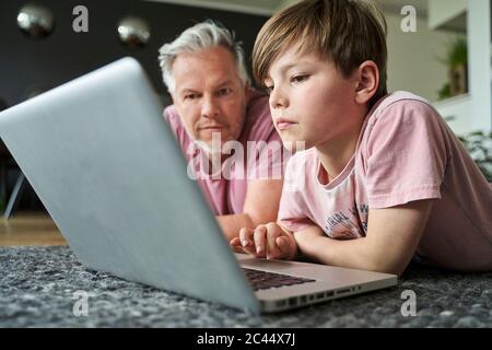 Padre e figlio si stendano sul pavimento, lavorando su un computer portatile Foto Stock