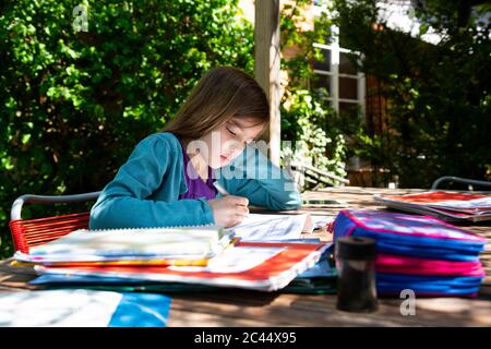 Ragazza seduta al tavolo da giardino facendo i compiti Foto Stock