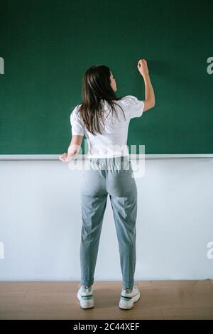 Vista posteriore completa della scrittura di giovani studentesse sulla lavagna in classe universitaria Foto Stock