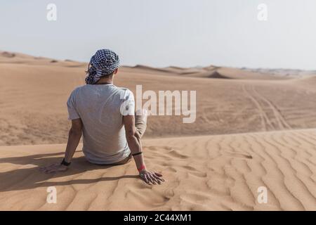 Giovane seduto sulle dune di sabbia nel deserto a Dubai, Emirati Arabi Uniti Foto Stock