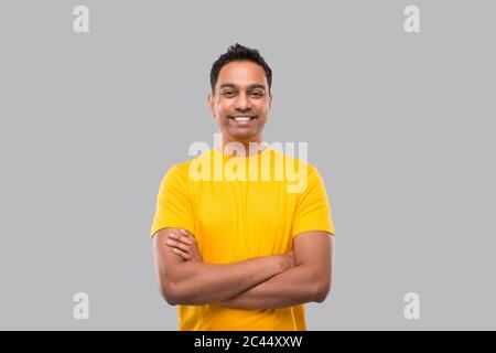 L'uomo indiano in piedi mani incrociate sorridendo in giallo TShirt isolato Foto Stock