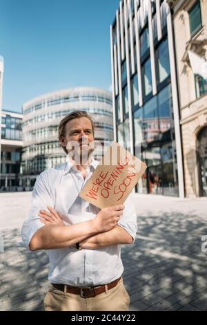 Negoziante in possesso di cartone con annuncio di apertura in città Foto Stock