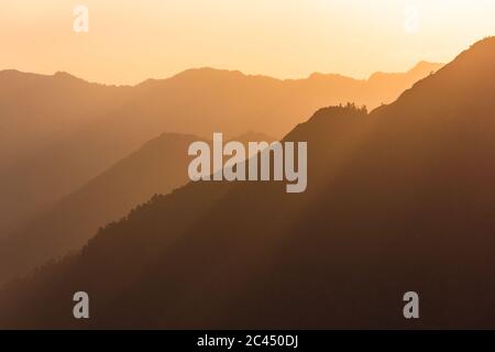 Raggi del sole che scorrono attraverso le silhouette di montagna nebbie nel villaggio Himalayan di Sarahan in Himachal Pradesh, India. Foto Stock