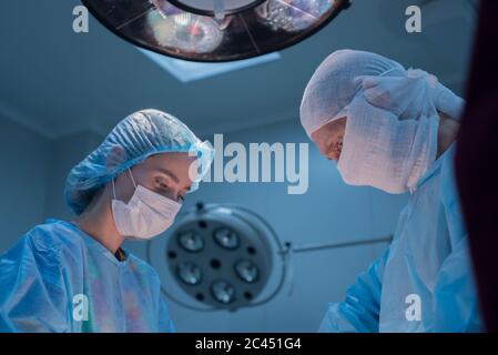 I chirurghi dei bambini eseguono la chirurgia urologica. Un uomo e una donna in una maschera, e un abito sterile blu, in sala operatoria. Vista dal basso Foto Stock