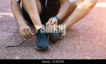 Millennial runner che legano i pattini mentre si siede sulla strada durante il suo addestramento, primo piano Foto Stock