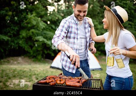 Coppia giovane la preparazione di salsicce su un barbecue all'aperto Foto Stock