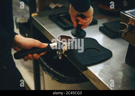 Barista preme il caffè macinato usando tamper. Vista da vicino su mani con portafilter Foto Stock