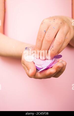 Mani per bambini con glitter e confetti di colore blu e argento su sfondo rosa pastello. Foto Stock