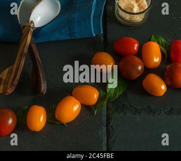 Pomodori ciliegini. Isolato. Pomodori ciliegini rossi e arancioni su una superficie di pietra nera. Immagine stock Foto Stock