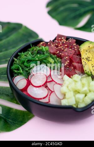 Vista dall'alto della ciotola di tonno con riso, avocado, wakame, ravanello e cetriolo su sfondo rosa Foto Stock