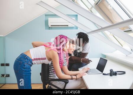 Due giovani donne e un giovane uomo seduti alla scrivania, guardando il computer portatile. Foto Stock