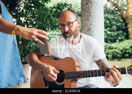 Uomo tatuato con capelli lunghi e occhiali che suonano la chitarra. Foto Stock