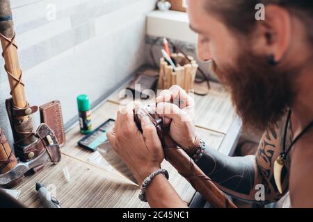 Uomo tatuato con bearded con lunghi capelli di brunetta seduti al tavolo, tenendo l'ascia con il legno e manico di cuoio. Foto Stock