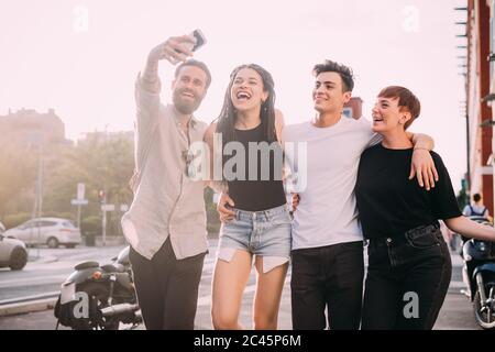 Due giovani donne e uomini che indossano abiti casual in piedi su un tetto, prendendo selfie con il telefono cellulare. Foto Stock