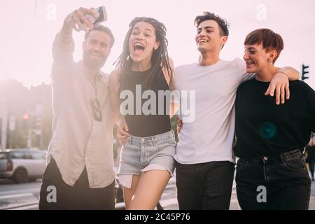 Due giovani donne e uomini che indossano abiti casual in piedi su un tetto, prendendo selfie con il telefono cellulare. Foto Stock