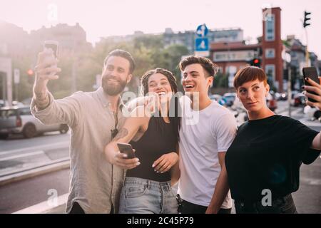 Due giovani donne e uomini che indossano abiti casual in piedi su un tetto, prendendo selfie con il telefono cellulare. Foto Stock