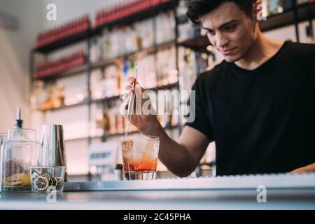 Giovane uomo che indossa abiti neri in piedi dietro il bancone bar, preparare la bevanda. Foto Stock